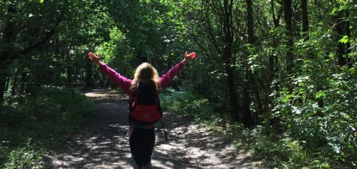 A woman with arms raised walking in the woods