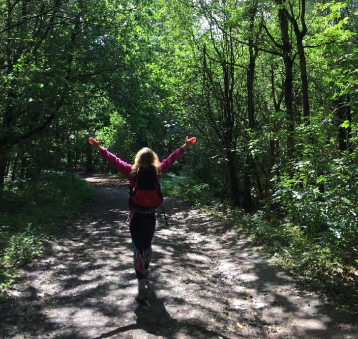 A woman with arms raised walking in the woods