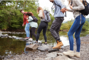 A group of teenagers using stepping stones to cross a stream