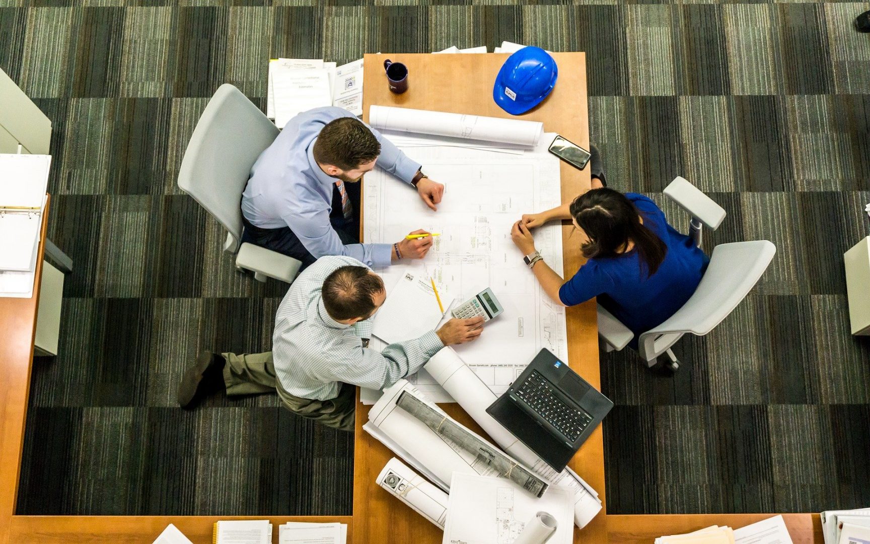 Three people gathered around a table studying a set of blueprints