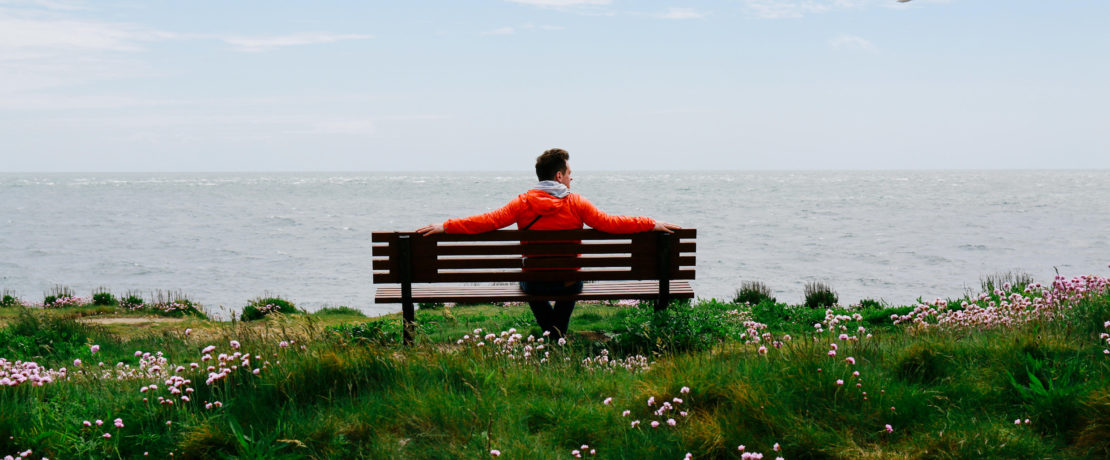 Man sitting on a coastal bench looking at the sea