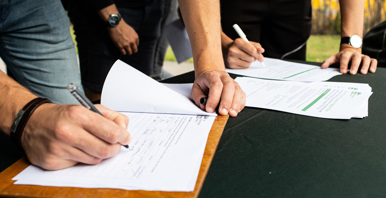 Close up of people's hands signing a form on a clipboard