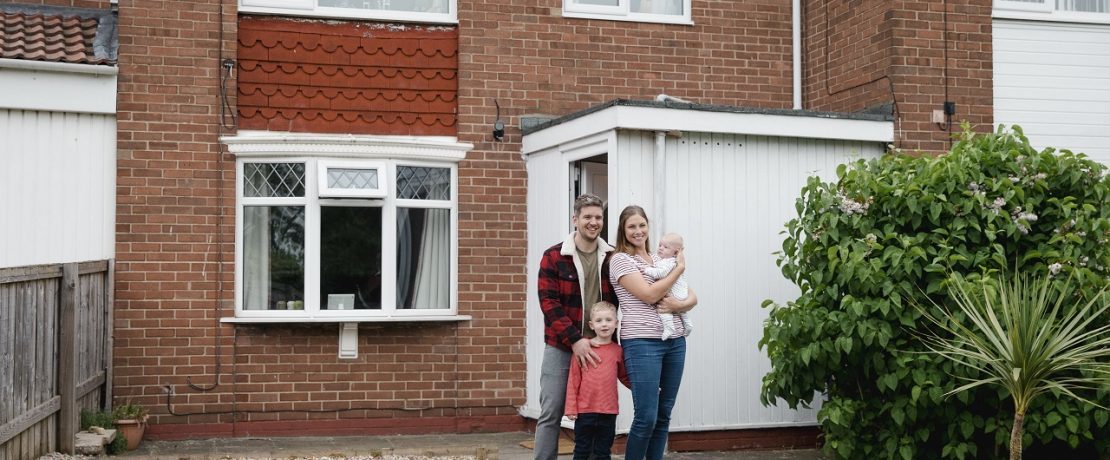 Family standing in front of a house and smiling