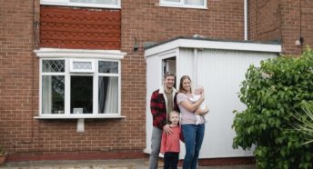 Family standing in front of a house and smiling