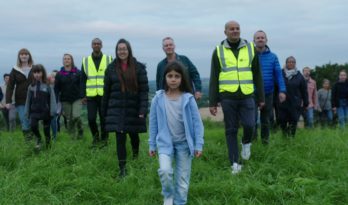 A crowd of people, lead by a young girl, walking across a field