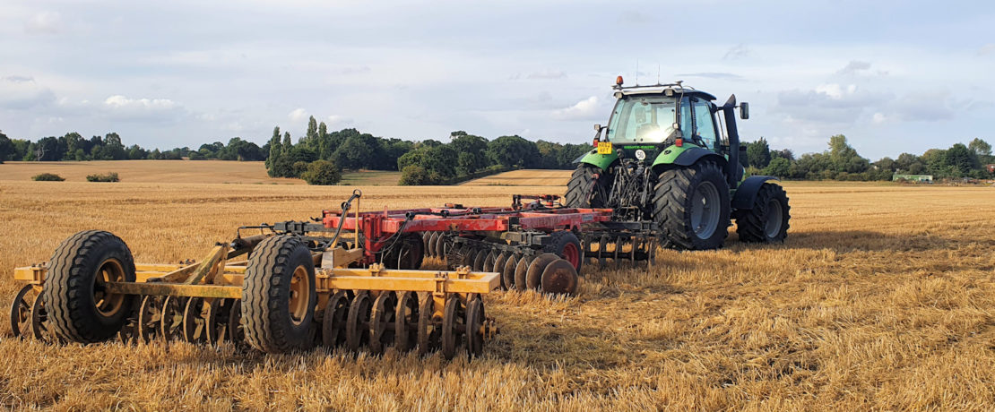 A tractor towing farm equipment on a recently harvested field