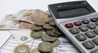 A calculator, payslip and small pile of GBP sterling notes and coins