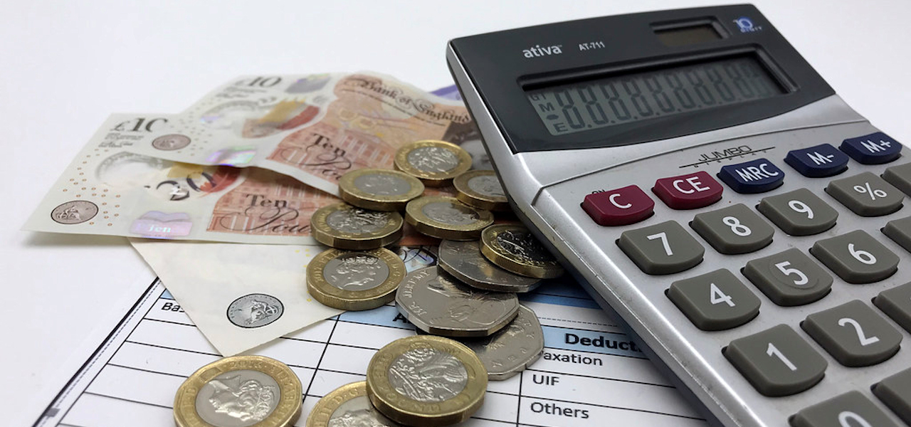 A calculator, payslip and small pile of GBP sterling notes and coins