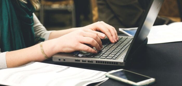 A person typing on a laptop with a smartphone next to them.