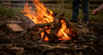 Close up shot of a bonfire with a hand adding extra twigs