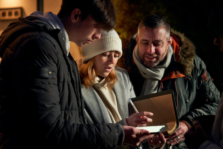 Father, son and daughter in winter, referring to a smartphone and taking notes in book