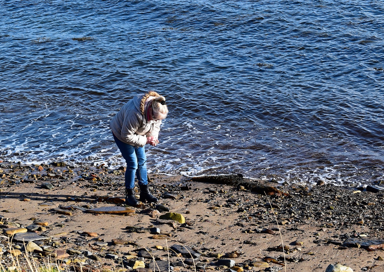 A woman beachcombing on the coastline on a pebbled beach next to the sea