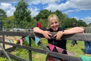 A woman smiling and leaning over a wooden 5-bar gate at Martha's Meadow