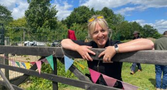 A woman smiling and leaning over a wooden 5-bar gate at Martha's Meadow