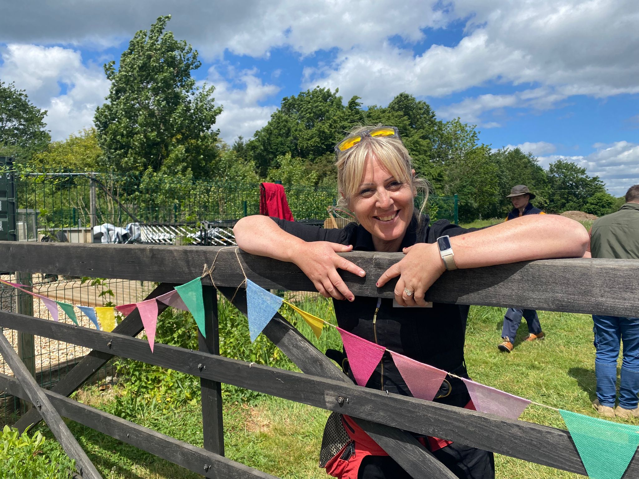 A woman smiling and leaning over a wooden 5-bar gate at Martha's Meadow