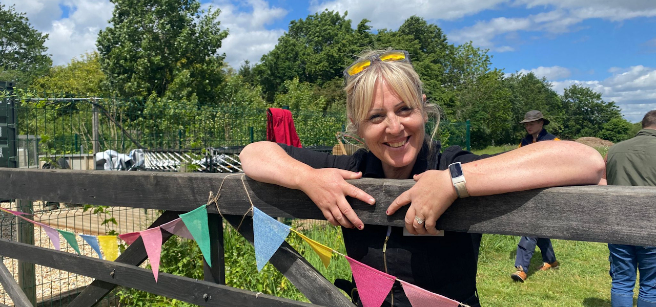 A woman smiling and leaning over a wooden 5-bar gate at Martha's Meadow