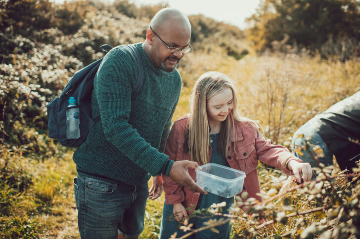 A man and young girl blackberries from a hedgerow on a family walk