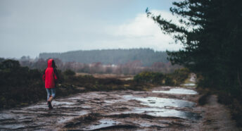 A woman in a red coat walking on a path in the countryside in the rain