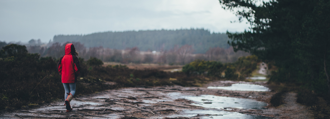 A woman in a red coat walking on a path in the countryside in the rain