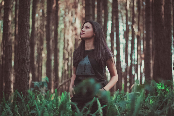 A woman standing in a forest of firs and ferns looking at the trees