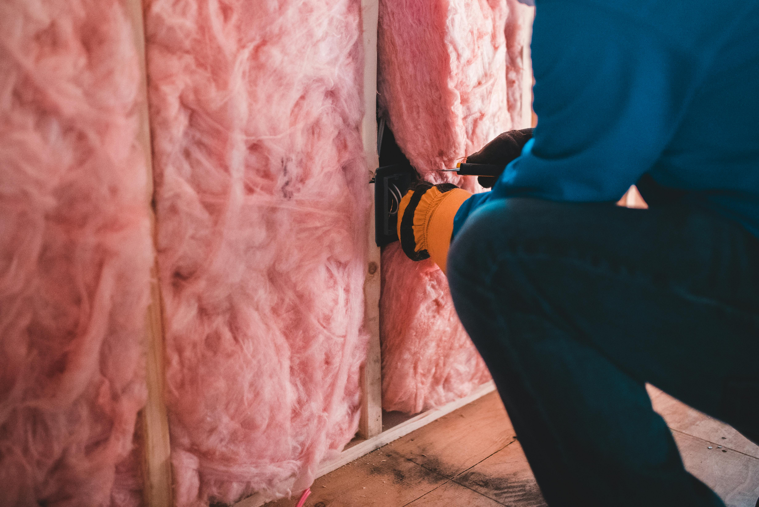 A worker insulating a wall with fibreglass insulation