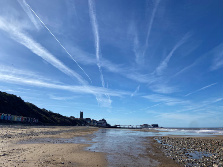 Cromer beach, showing the wide expanse of sand, blue sky above and Cromer Pier in the distance.