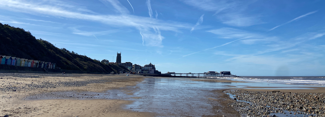 Cromer beach, showing the wide expanse of sand, blue sky above and Cromer Pier in the distance.