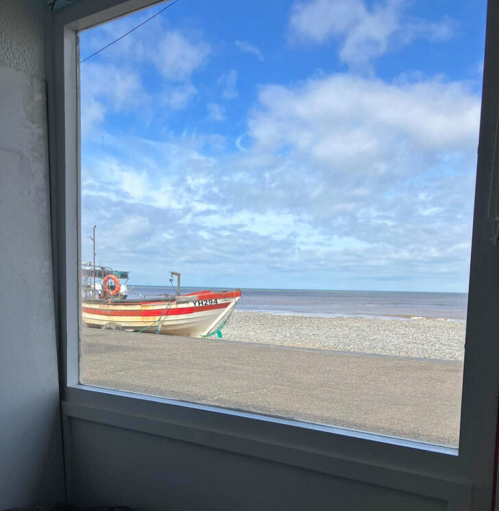 Cromer beach and a crabbing boat moored on the sand, as seen through the window of a beach hut.
